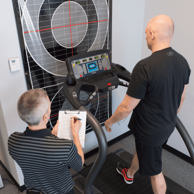 a man standing on a treadmill, with another man standing next to him, both of them engaged in a conversation