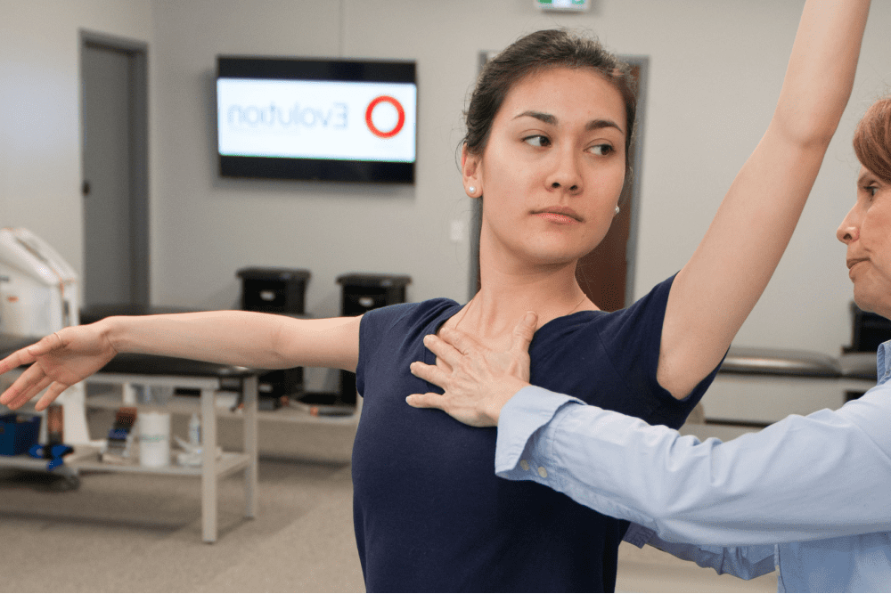 a woman in a blue shirt, standing in a room with her arms stretched out